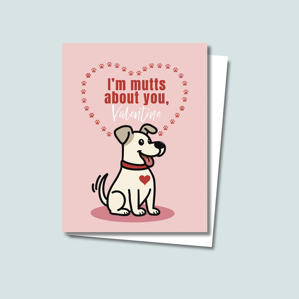 Mutts About You Valentine's Day card featuring cute tan dog with brown ears has a red heart on chest and is wearing a red collar, the dog is sitting on a dark pink round shadow and card has a muted pink background, red dog paws form a heart-shape above and behind the dog with text inside reading "I'm mutts about you, Valentine"
