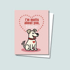 Mutts About You Valentine's Day card featuring cute tan dog with brown ears has a red heart on chest and is wearing a red collar, the dog is sitting on a dark pink round shadow and card has a muted pink background, red dog paws form a heart-shape above and behind the dog with text inside reading "I'm mutts about you, Valentine"