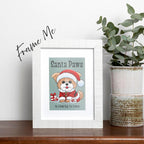 framed Santa Paws Christmas card featuring an adorable fluffy brown puppy in a Santa suit and hat sitting in snow next to a red and white wrapped gift, puppy's paw pads are red, text on top of card reads "Santa Paws", text on bottom of card reads "is coming to town", card has a muted teal background