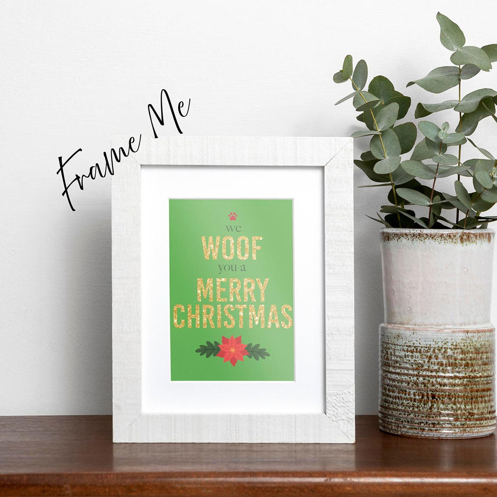 Framed We Woof You a Merry Christmas holiday card featuring Woof and Merry Christmas in gold-glitter-style text, we and you a are in a dark green text, a red paw print is on top of the card and a red poinsettia is on the bottom of the card, the background is green, frame not included in purchase