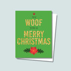 We Woof You a Merry Christmas holiday card featuring Woof and Merry Christmas in gold-glitter-style text, we and you a are in a dark green text, a red paw print is on top of the card and a red poinsettia is on the bottom of the card, the background is green