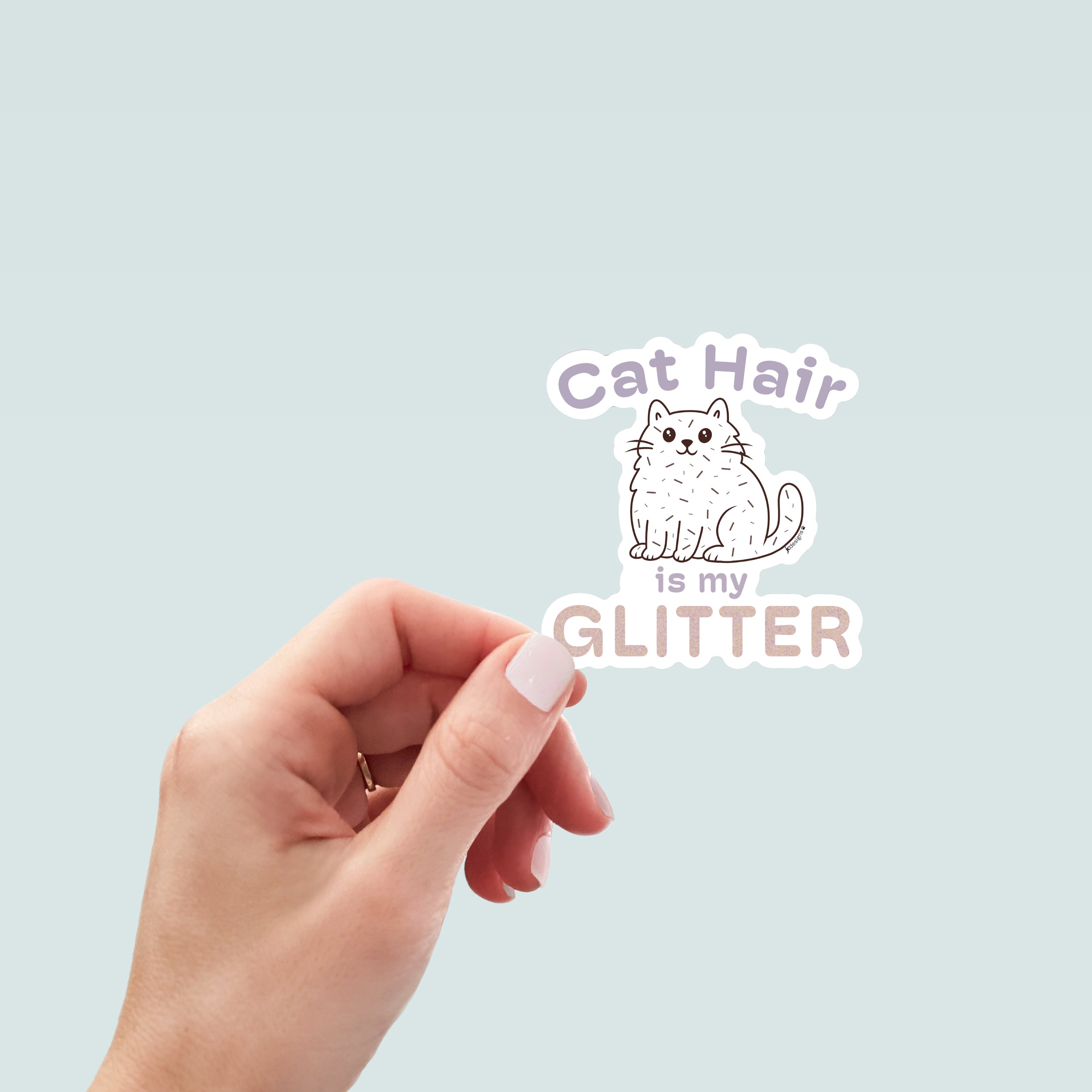 Hand holding a sticker of a fluffy white cartoon cat covered in scattered strands of cat hair. Above the cat, the phrase 'Cat Hair' is written in soft purple text, with 'is my' is smaller matching text below the cat. The word 'GLITTER' is prominently displayed at the bottom in large, sparkling textured letters. The design is outlined in white.