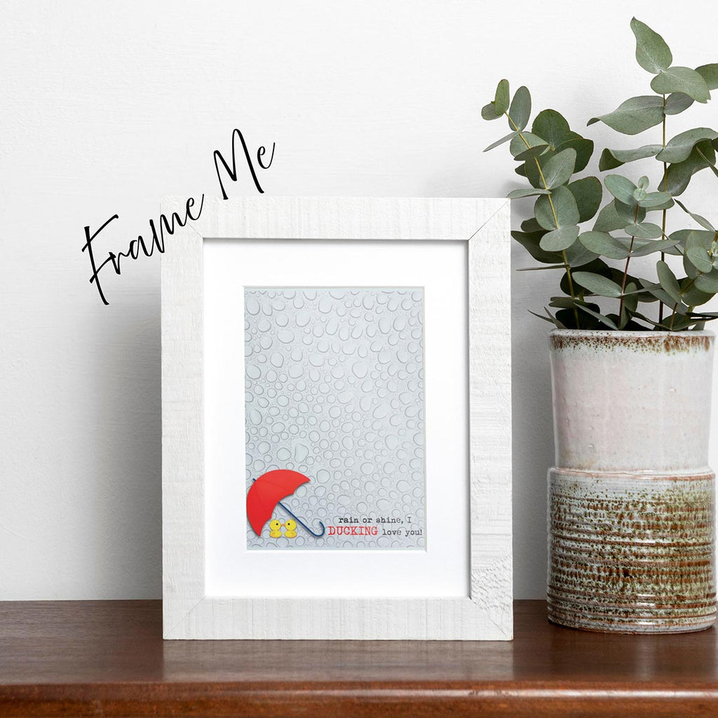 framed I Ducking Love You greeting card featuring two cute yellow ducks under a red umbrella with raindrop background, typewriter style text in bottom center to right reads "rain or shine, I ducking love you!" Ducking is in all caps and red color, the rest of the text is lower case and in black color, frame does not come with purchase