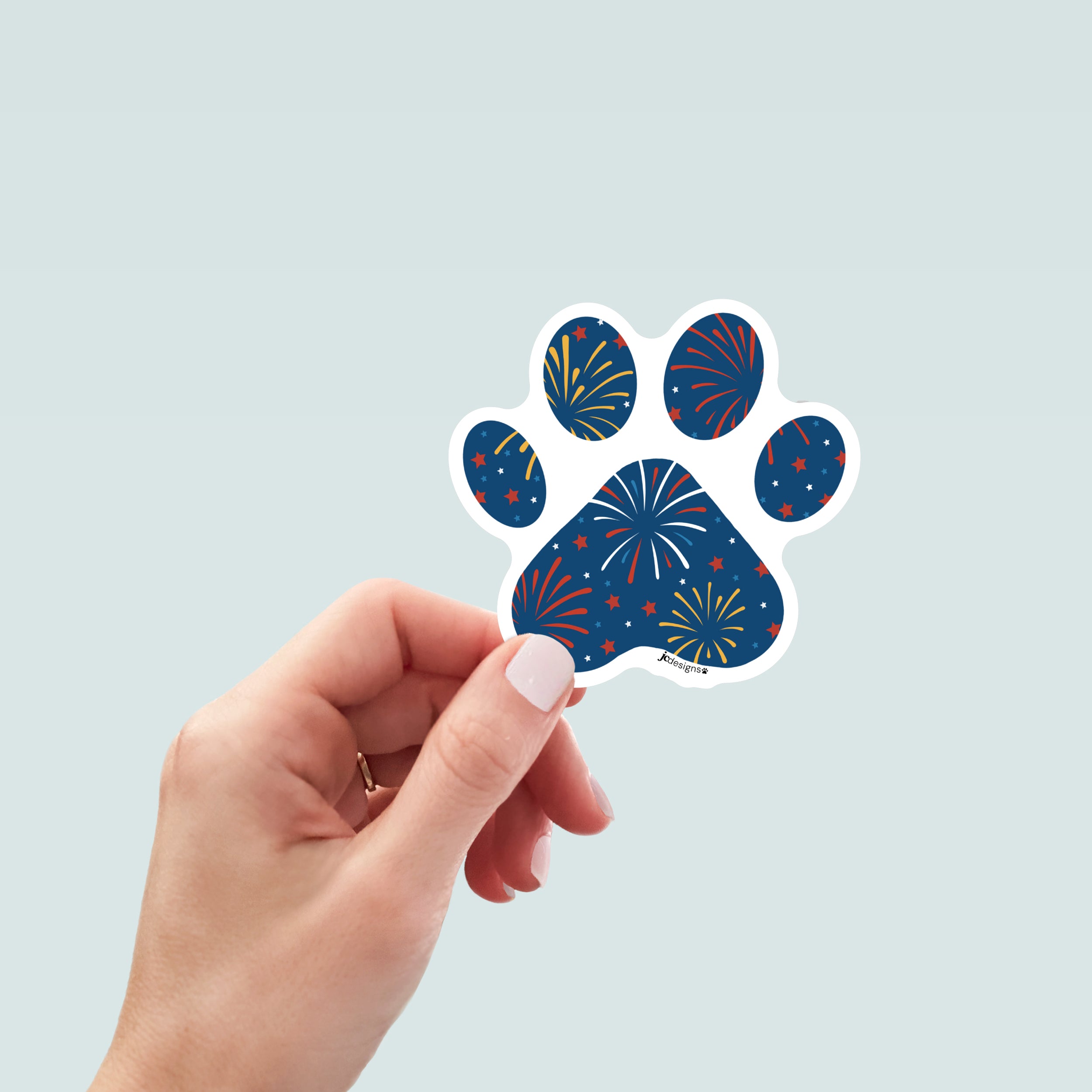Hand holding a paw-shaped sticker with fireworks design on a dark blue background