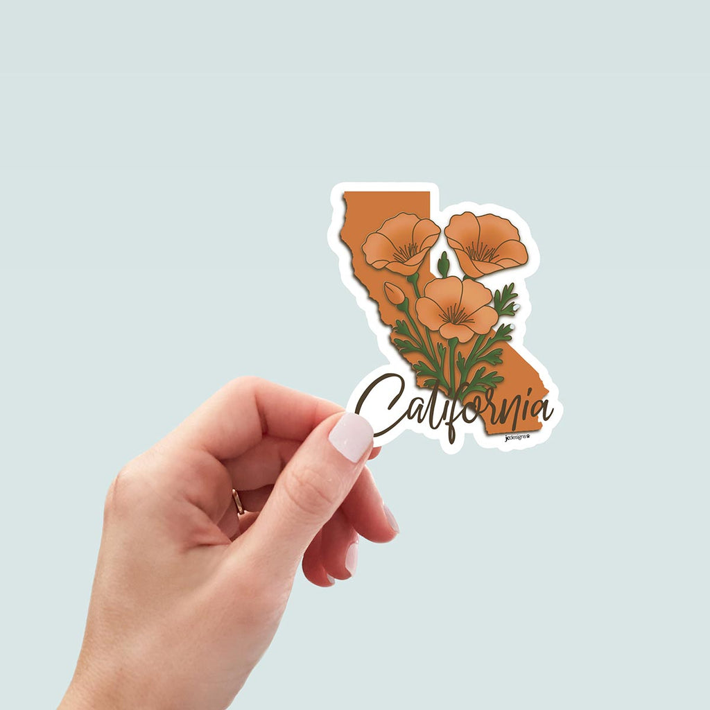 hand holding California state-shaped sticker featuring vibrant orange poppy flowers extending out of state outline with elegant script text reading "California" at bottom of sticker, white outline die cut