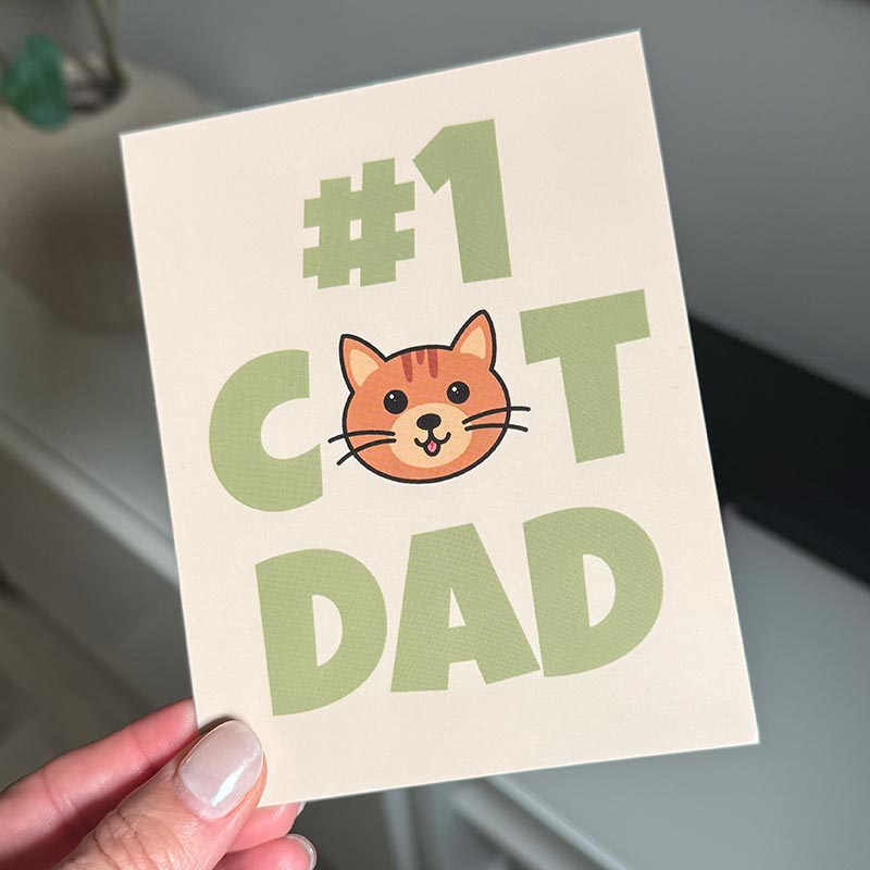 hand holding Father’s Day card featuring a cat illustration and the text “#1 Cat Dad”