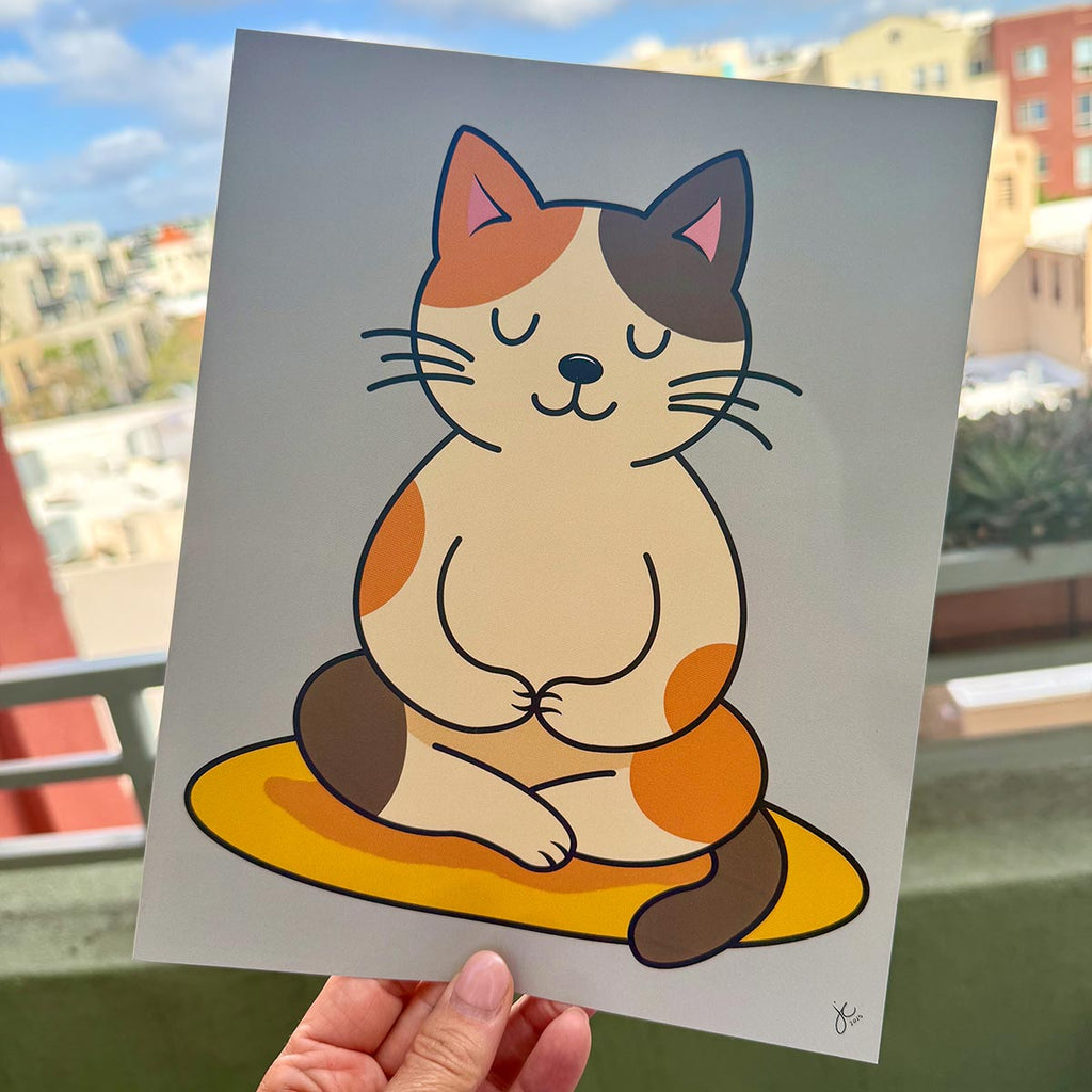 hand holding minimalist cat yoga art print featuring brown tan and orange calico cat sitting cross-legged in a meditative post on a yellow mat with muted blue green background