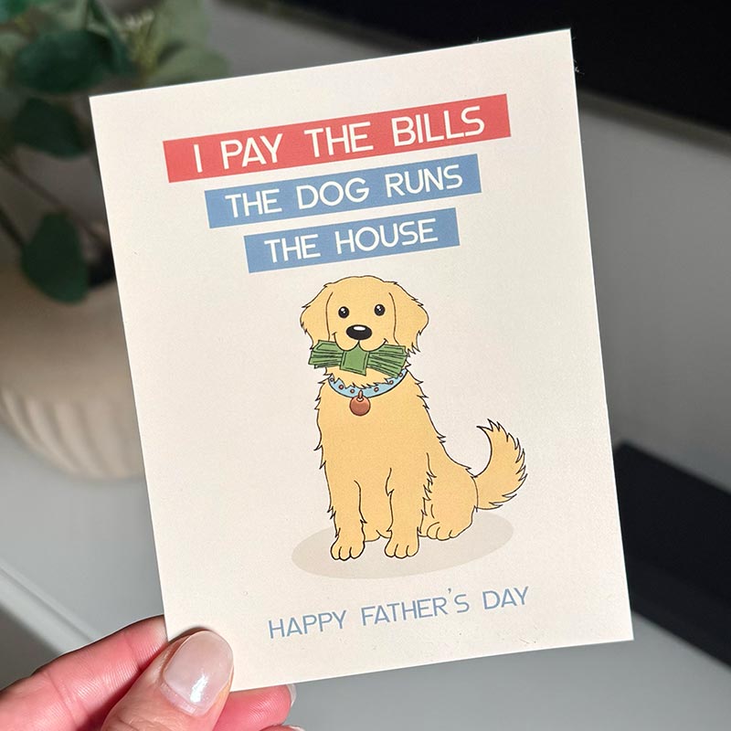 hand holding Funny Father’s Day card showing a dog holding money with the text “I pay the bills, the dog runs the house”