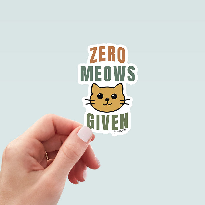 hand holding Zero meows given cat sticker featuring a cute cat face and bold playful typography in earthy colors, designed by JC Pet Designs