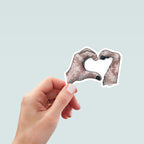 Hand holding sticker featuring hand and dog paw forming heart shape together in tan marble textured pattern.