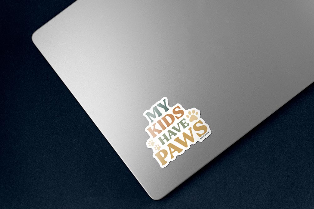 My kids have paws sticker with bold hand-lettered text and paw print details for proud pet parents, cat dads, dog moms, sticker on lower left corner of silver laptop
