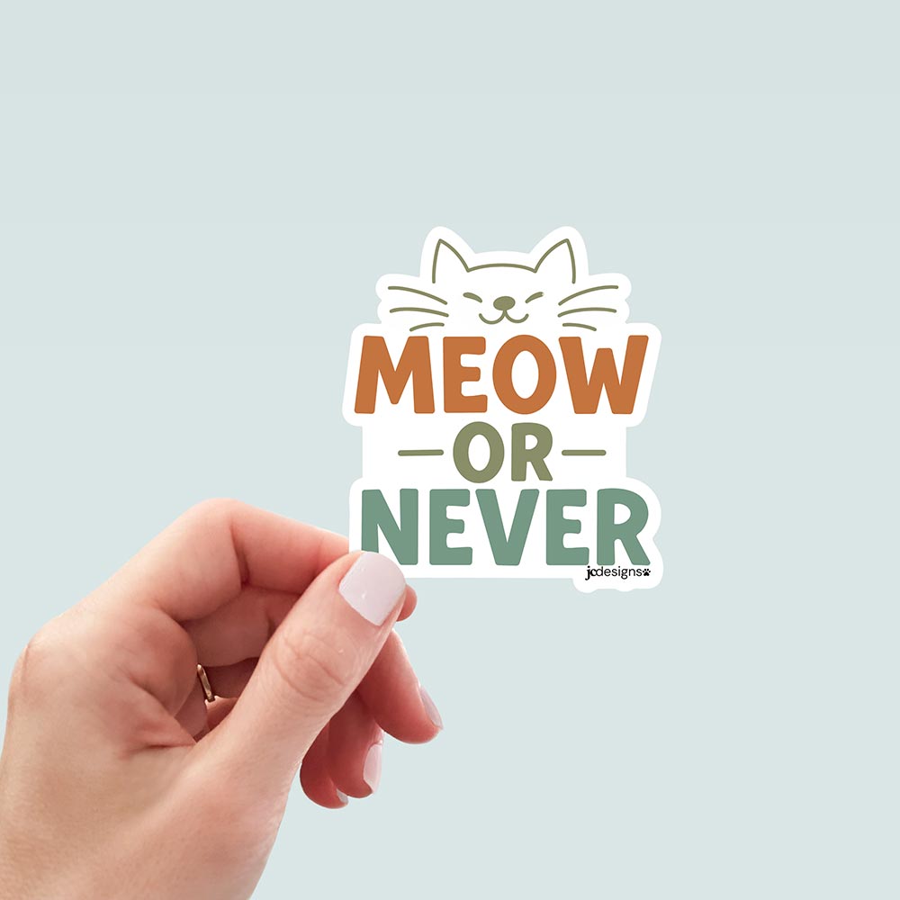 hand holding Meow or Never cat sticker with playful typography and a smiling cat face illustration in warm earthy colors, designed by JC Pet Designs