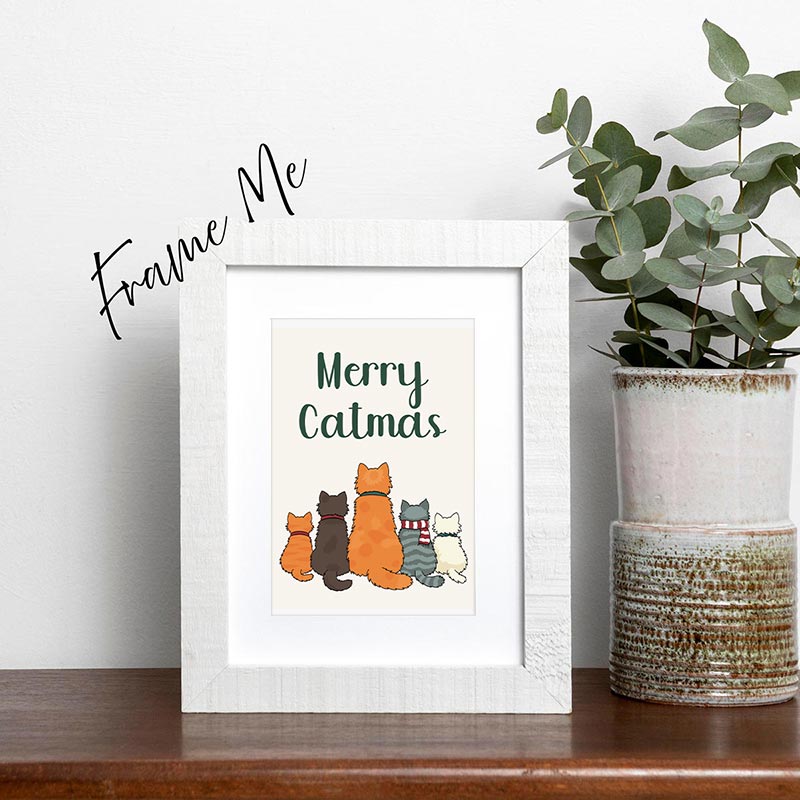 Framed print with 'Merry Catmas' text and cat illustrations on a shelf with a plant.