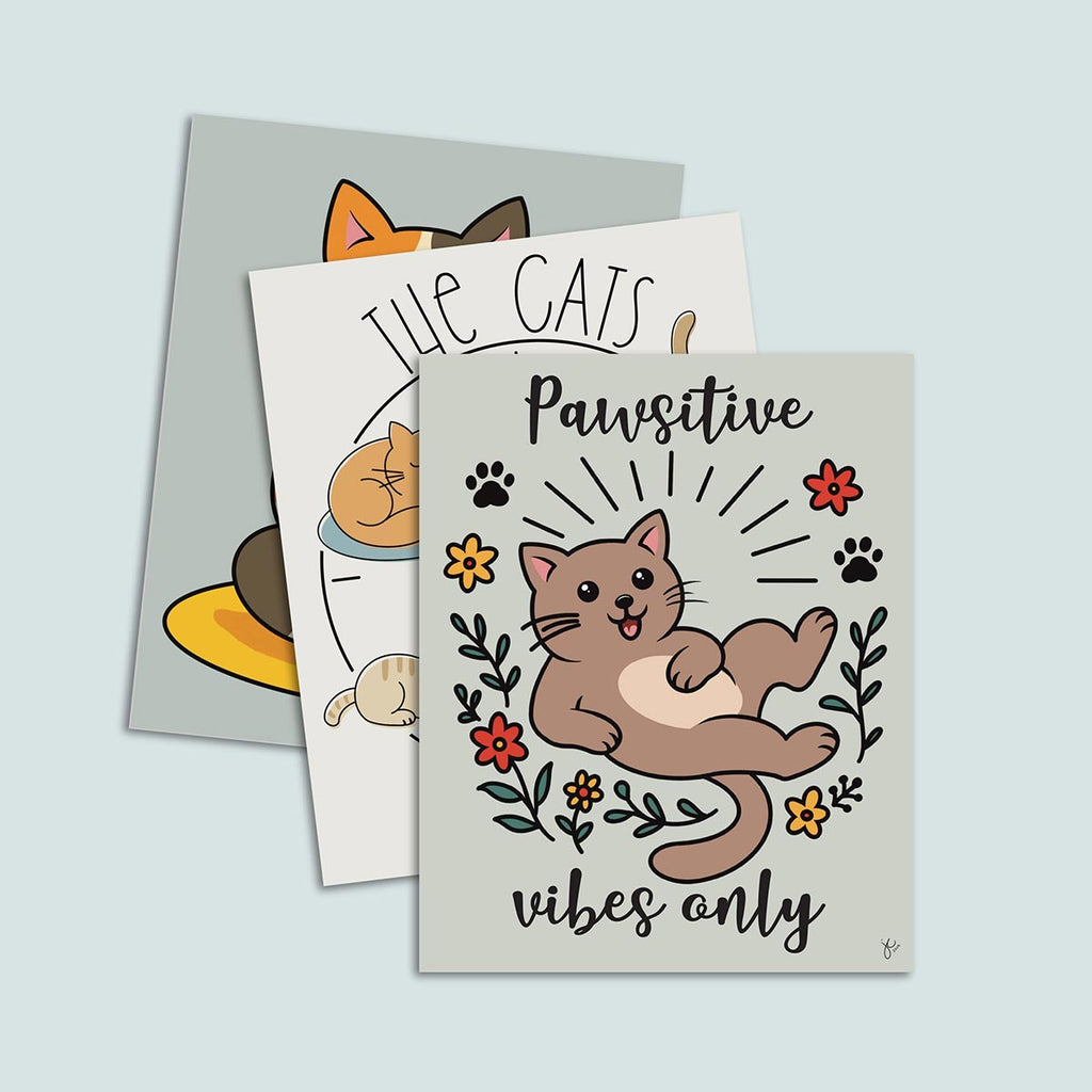 Set of three cat prints stacked, featuring on top Pawsitive Vibes Only art print featuring happy cartoon brown cat surrounded in a circle of red and yellow flowers and black paw prints with words Pawsitive on top and vibes on bottom print is on a light muted green background