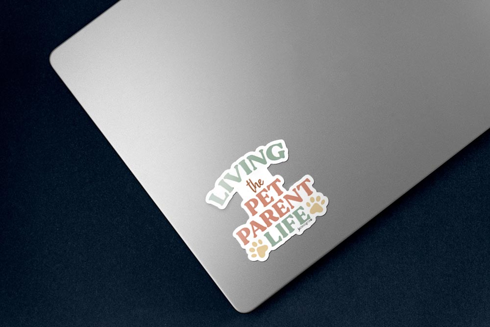 living the pet parent life sticker with modern typography and paw print accents in earthy pastel colors perfect for cat dad, dog mom, sticker on lower left corner of silver laptop