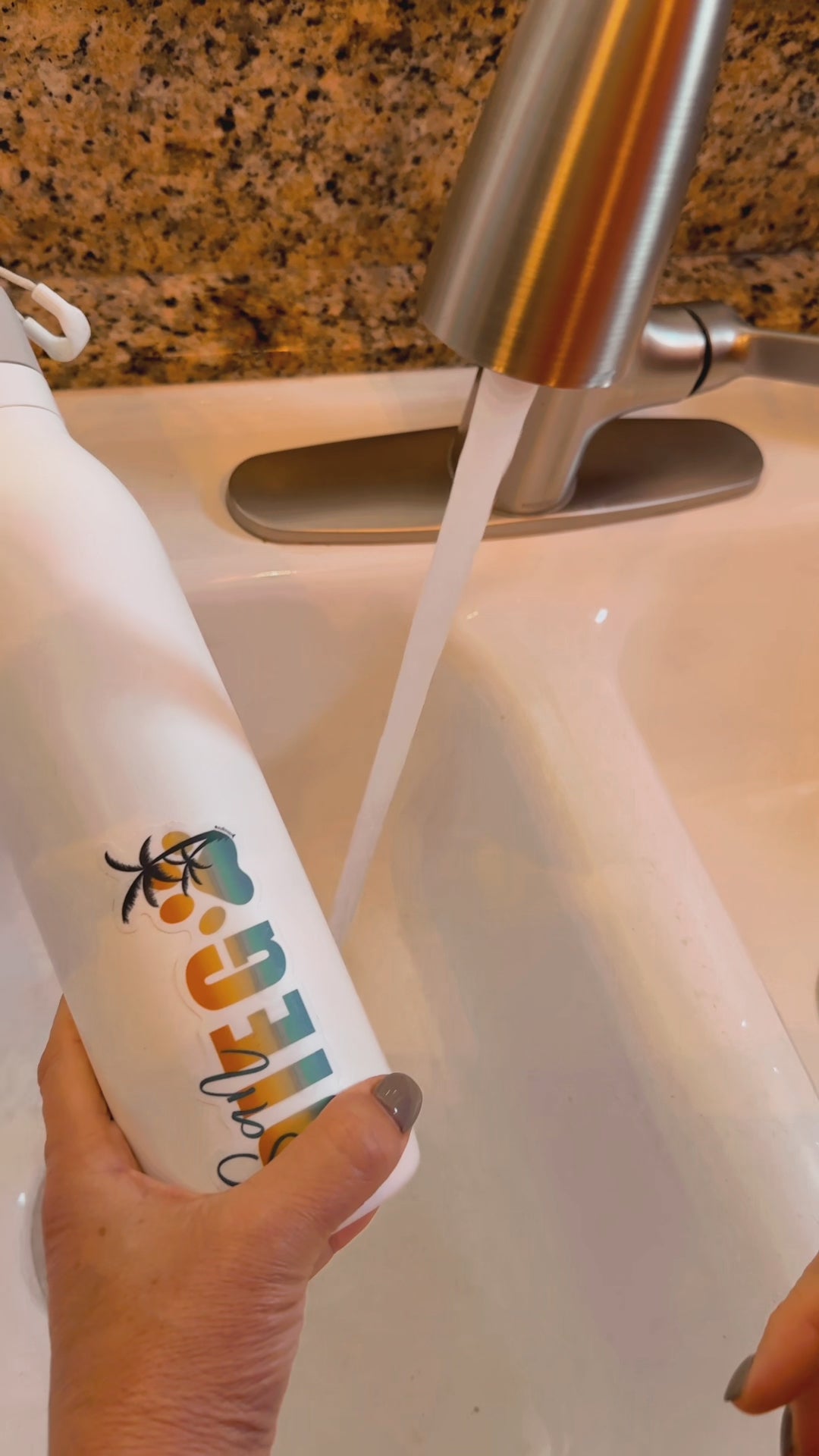 video of hand holding waterproof pet-themed vinyl sticker on a white bottle being rinsed under a running faucet, demonstrating durability and long-lasting quality from JC Pet Designs
