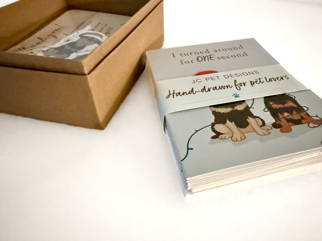 stack of hand-drawn custom greeting cards with dog illustrations next to a cardboard box on a white surface